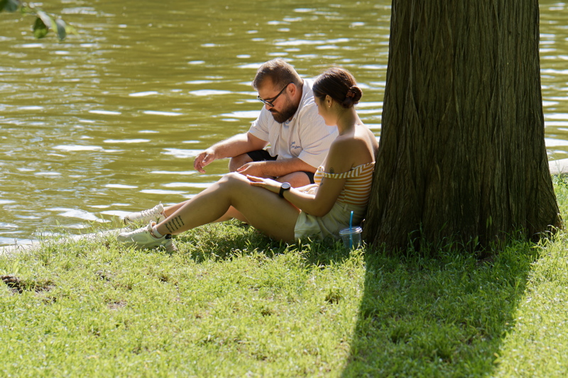 16 - Two individuals relaxing together on a grassy riverbank near a large tree